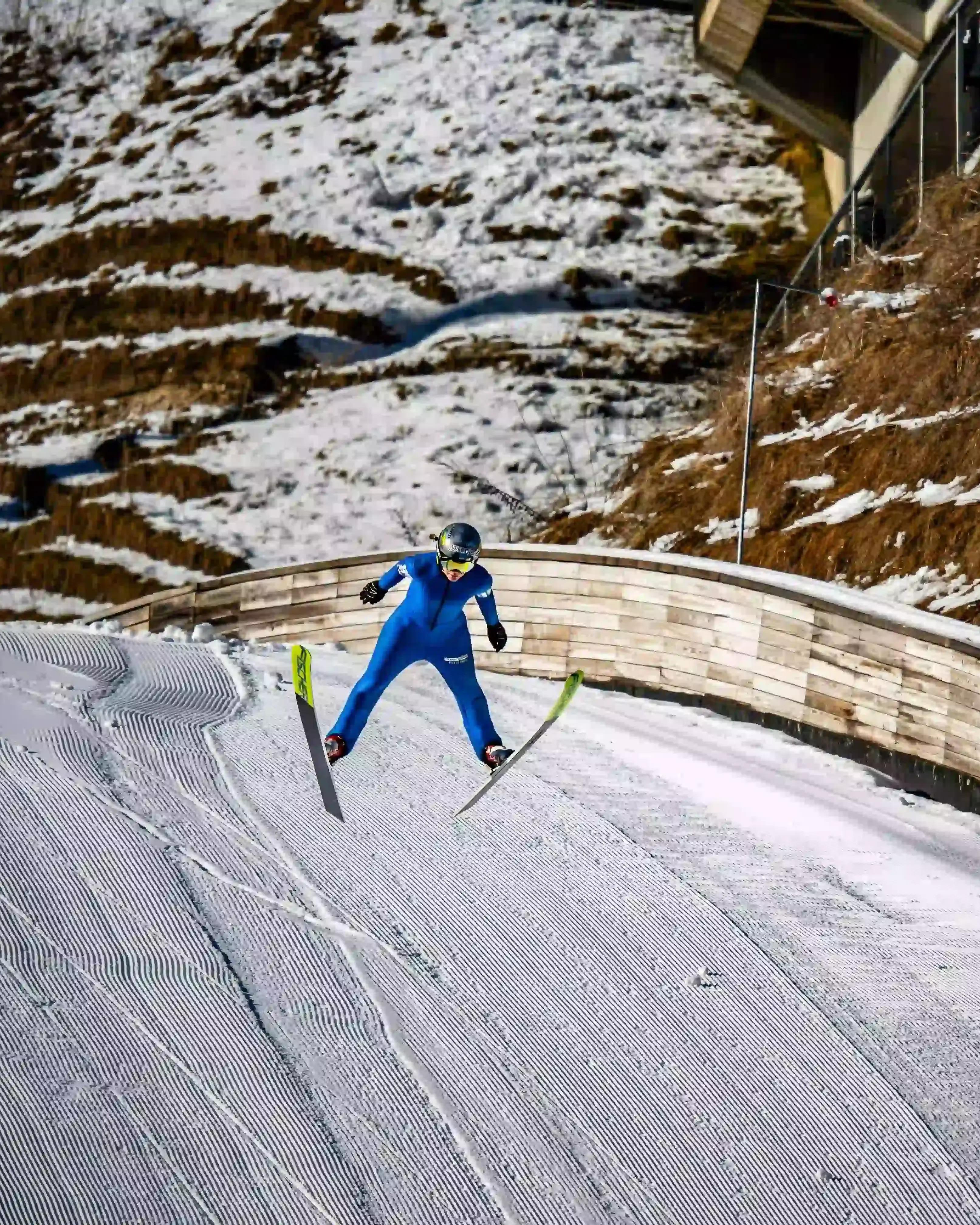Saltador de esquí en pleno vuelo durante una competición de deportes de invierno en una pista alpina preparada.