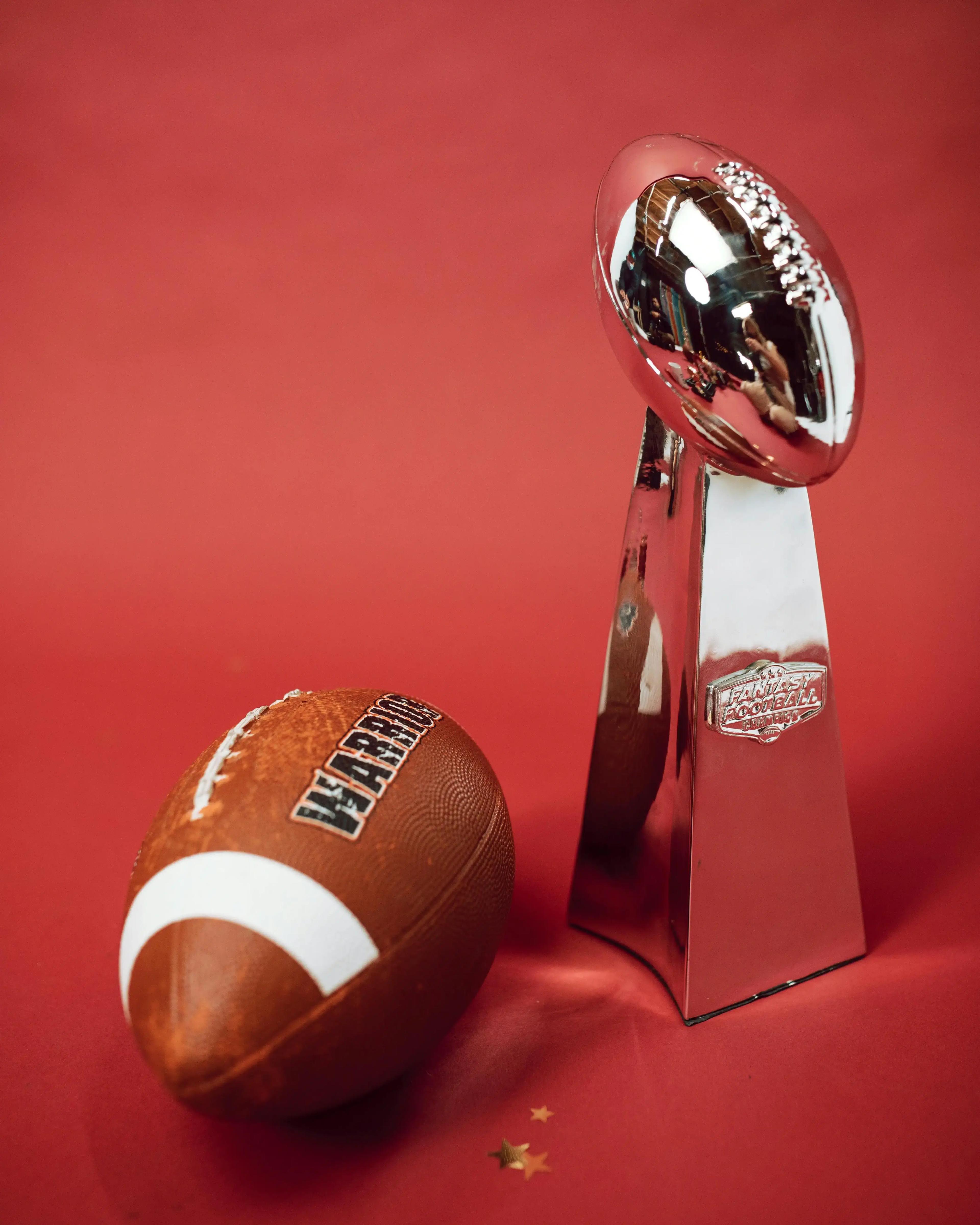 Football americano accanto a un trofeo del campionato su sfondo rosso.