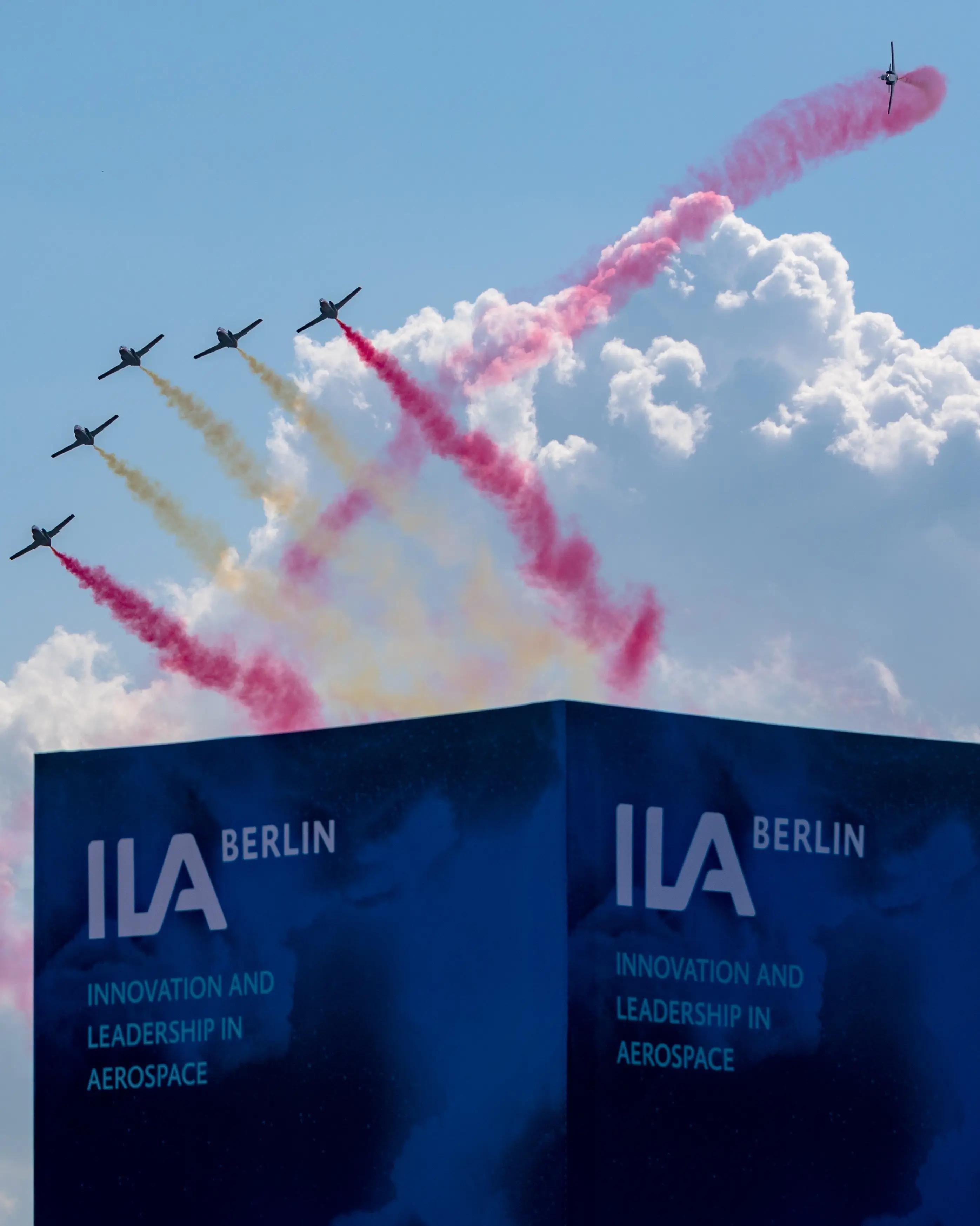 Kunstflugzeuge fliegen über der ILA Berlin mit farbigen Rauchfahnen am Himmel.